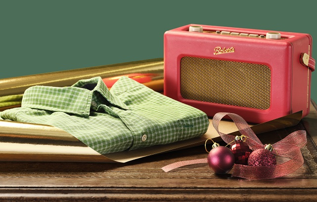 A folded green checked shirt and a vintage red radio on top of wrapping paper, next to red Christmas baubles.